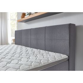 Boxspringbett mit grauem Stoffbezug und gepolstertem Kopfteil mit quadratischer Steppung