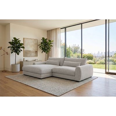 Milieubild eines weißen Ecksofas mit linker Ottomane, breiten Armlehnen und schwarzen Kunststofffüßen in einem hellen Wohnzimmer mit großen Fensterflächen