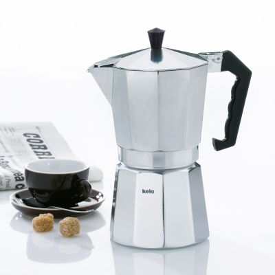 Silberfarbener Espressobereiter auf hellem Untergrund neben kleinen Kaffeetassen und gerösteten Kaffeebohnen