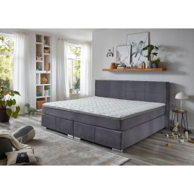 Boxspringbett mit grauem Stoffbezug und Matratze mit Topper in einem hellen Schlafzimmer