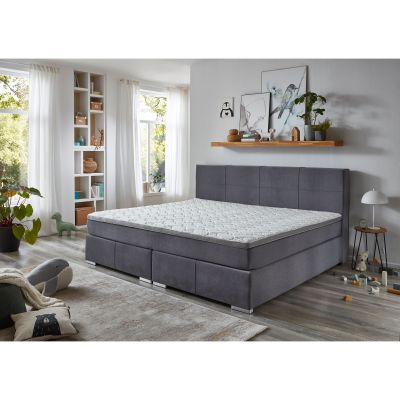 Boxspringbett mit grauem Stoffbezug und Matratze mit Topper in einem hellen Schlafzimmer