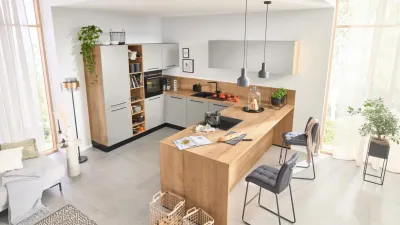 Überblick einer modernen Interliving Küche aus 45-Grad-Perspektive mit heller Holzoptik, hellgrauen Fronten und schwarzen Griffen
