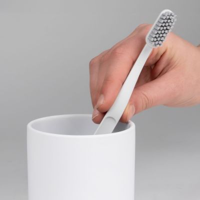 Nahaufnahme einer Hand beim Einsetzen mehrerer Zahnbürsten in einen weißen zylindrischen Becher