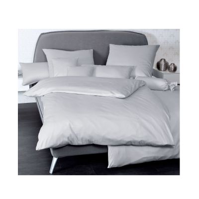 Bett mit Janine Mako-Satin Bettwäsche Colors 31001 in Platin, arrangiert mit mehreren Kissen in einem hellen Schlafzimmer.