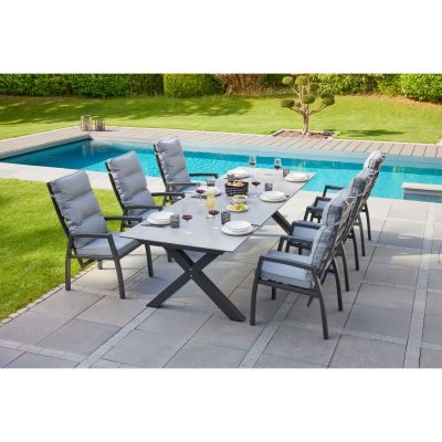 Mehrere Gartenstühle mit Polstern stehen um einen Tisch auf einer gepflasterten Terrasse neben einem Pool