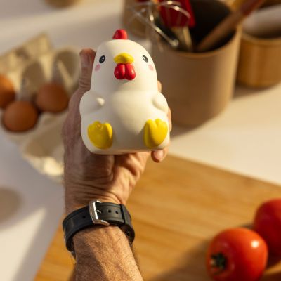 Weiße Antistress-Figur in Hühnerform, in einer zweiten Aufnahme über der Küchenarbeitsfläche in der Hand gezeigt.