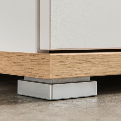 Nahaufnahme des unteren Sockelbereichs einer weißen Garderobenkommode mit Holzabsetzung und eckigem Metallfuß