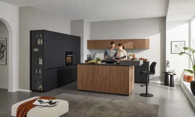 Fröhliches Paar kocht in moderner griffloser Interliving Küche mit anthrazitfarbenen Fronten, markantem Holz und Barhockern