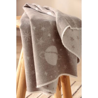 Babydecke Universe taupe hängt über einer Stuhllehne und zeigt weiße Mond- und Sternmotive auf taupefarbenem Stoff.