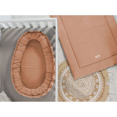 Rostbraunes Babynest aus Musselin in einem weißen Kinderbett neben passender Krabbeldecke auf rundem Teppich mit Mandala-Muster