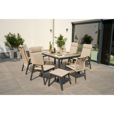 Stilvolles Gartenmöbel-Set mit Tisch, Stühlen und Hocker auf sonniger Terrasse, umgeben von Pflanzen und Glasfront.