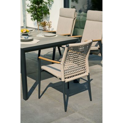 Ein Stuhl mit Geflecht-Rückenlehne und Sitzpolster steht an einem rechteckigen Gartentisch, im Hintergrund weitere Stühle und Pflanzen.