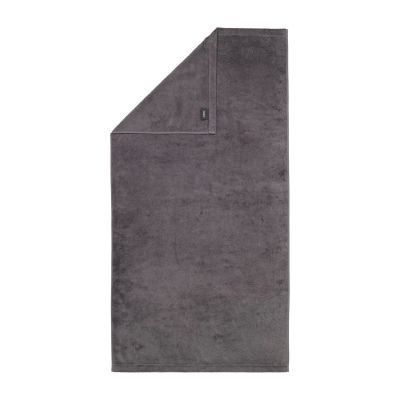 Duschtuch in der Farbe Anthrazit mit umgeschlagener Ecke; Rückseite, Saum und kleines Textiletikett sind auf weißem Hintergrund sichtbar.