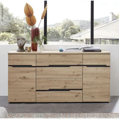 Holzsideboard vor großer Fensterfront; darauf Vasen, eine Pflanze, eine Sanduhr und ein geöffnetes Buch.
