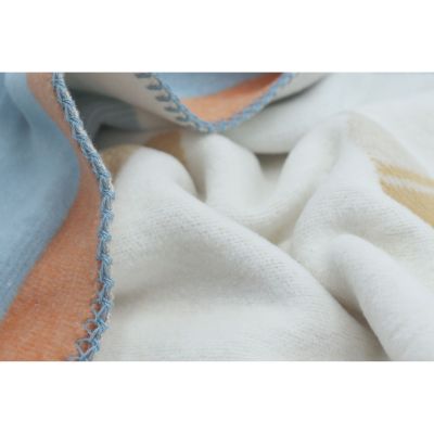Nahaufnahme der Babydecke Orbit mit cremefarbenen Stofffalten und blau-orange eingefasstem Rand.