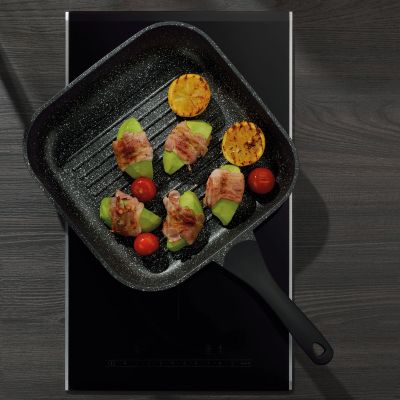 Schwarze quadratische Grillpfanne mit Tomaten Paprika Zucchini und weiterem Gemüse auf einem dunklen Kochfeld