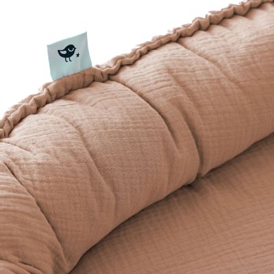 Nahaufnahme eines rostbraunen Babynests aus Musselin mit gerafftem Rand und kleinem Etikett mit Vogelmotiv
