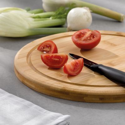 Hellbraunes Schneidebrett mit geschnittenen Tomaten und schwarzem Küchenmesser neben frischem Gemüse