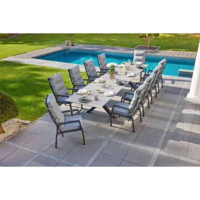 Mehrere Gartenstühle mit Polstern stehen um einen rechteckigen Tisch auf einer Terrasse neben einem Pool