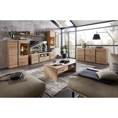 Moderner Wohnraum mit Couchtisch aus hellem Holz, Sofas und einer beleuchteten Wohnwand; große Fenster geben den Blick auf Außenbereich und Natur frei.