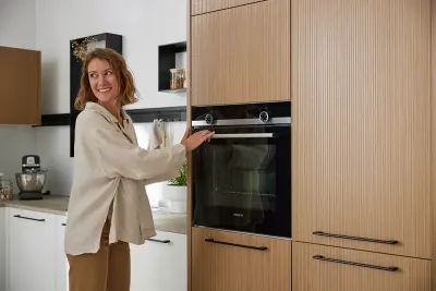 Frau bedient integrierten Backofen in klassischer Interliving Küche mit Holzfronten und weißen Unterschränken