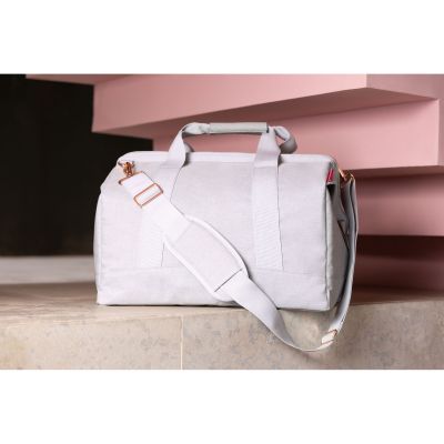Reisetasche von Reisenthel, Modell Allrounder L, in sehr hellem Grau mit rosafarbenen Details, in einem Innenraum auf einer niedrigen Ablage unter einer Treppe.