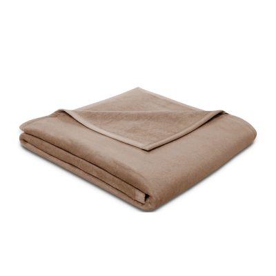 Gefaltete Wohndecke CottonSense palisade in warmem Taupe mit schmal eingefasster Kante auf weißem Hintergrund.