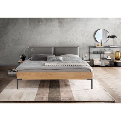 Bett mit gepolstertem Kopfteil und Holzrahmen in einem Schlafzimmer mit zwei Nachttischen und grauer Wand im Hintergrund
