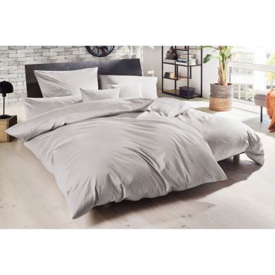 Silberne Bettwäsche auf einem bezogenen Doppelbett mit mehreren Kissen im Schlafzimmer