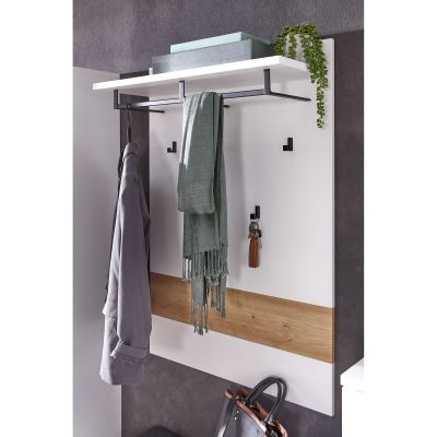 Nahaufnahme eines weißen Wandpaneels mit Ablage und Haken, an denen Jacke, Schal und Schlüssel hängen; oben stehen zwei Boxen und eine hängende Pflanze.