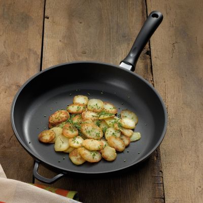 Schwarze Bratpfanne mit goldbraun gebratenen Kartoffelscheiben und grünen Kräutern