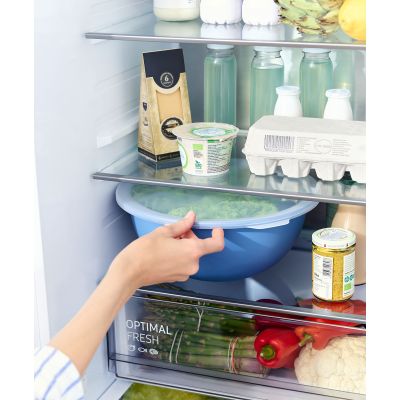 Hand hält eine blaue Rührschüssel mit transparentem Deckel in einem Kühlschrank