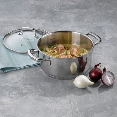 Geöffneter silberfarbener Bratentopf mit einem zubereiteten Gericht neben Glasdeckel, Knoblauch und roten Zwiebeln