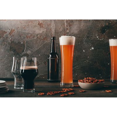 Hohes Beer-Basic-Weizenbierglas mit Bier in einer dunklen Tischszene, neben weiteren Gläsern und Gefäßen.