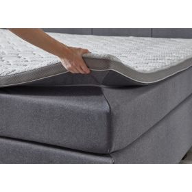 Boxspringbett mit grauem Stoffbezug während ein Topper an der Ecke angehoben wird