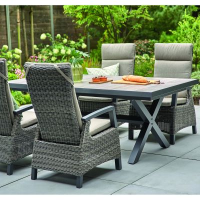 Nahansicht im Garten, Tisch mit Holzoptik-Platte und vier Stühlen aus Polyrattan mit Kissen, gedeckt mit Brot und Getränken.