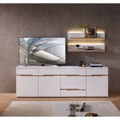 Wohnzimmeransicht mit einem weißen Sideboard. Darauf steht ein Fernseher. An der Wand darüber hängen zwei beleuchtete Wandregale mit Dekoration. Rechts auf dem Sideboard liegen Bücher und Dekoobjekte, im Vordergrund ein Couchtisch.