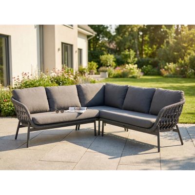 graue Gartenlounge mit Ecksofa und Kissen steht auf einer Terrasse vor einem Garten mit Bäumen und Pflanzen
