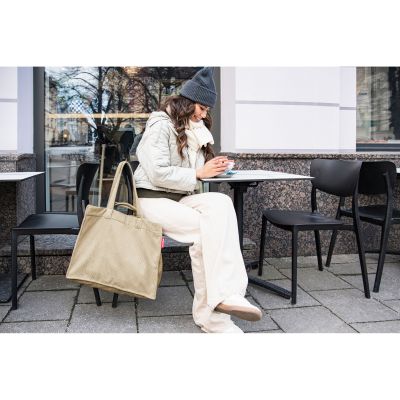 Frau sitzt mit beigem Reisenthel Cord-Shopper vor einem Café im Außenbereich und hält eine Tasse in der Hand