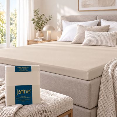 Sandfarbenes Janine Topper-Spannbetttuch 5001 liegt glatt auf dem Topper eines Boxspringbetts; die Verpackung ist im Vordergrund zu sehen.