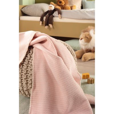 Babydecke Cotton rose liegt in einem Kinderzimmer über einem Möbelstück; Stofftiere und Spielzeug stehen im Hintergrund.