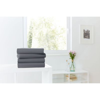 Vier gefaltete Spannbetttücher in Anthrazit auf einer weißen Kommode vor einem hellen Fenster; Größe 100 x 200 x 30 cm.