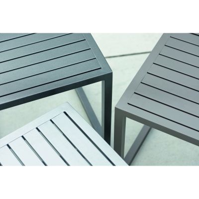 Schräg von oben aufgenommene Detailansicht von drei quadratischen Metalltischen, Fokus auf Tischplatten mit Längsrillen und rechtwinklige Ecken.