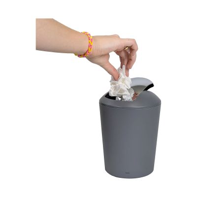 Eine Hand wirft Abfall durch den geöffneten Schwingdeckel in den grauen Eimer
