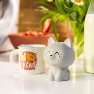 Graue Antistress-Figur in Katzenform, neben einer Tasse und einer Pflanze auf einem Tisch dargestellt.