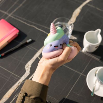 Pastellfarbene Antistress-Figur in Häufchenform mit Einhornhorn, in einer zweiten Perspektive über dem gedeckten Tisch gehalten gezeigt.