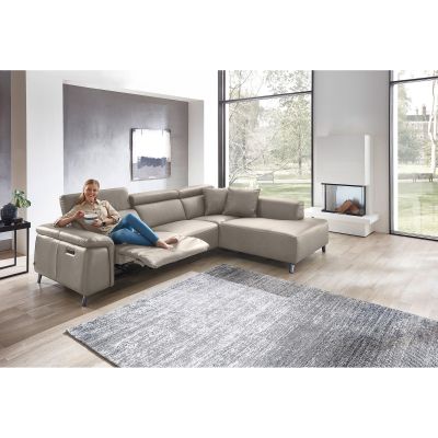 Frau entspannt auf beigem Ecksofa mit ausgeklappter Relaxfunktion in hellem Wohnzimmer mit Kamin und Teppich