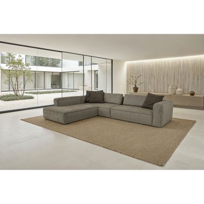 Die ca. 230 x 330 cm große Eckgarnitur in Dunkelbraun steht frei auf einem Teppich in einem hellen, modernen Wohnraum. Die lange Ottomane ist links angeordnet und das Sofa ist mit dunklen Dekokissen ausgestattet.
