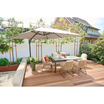 Gartentisch mit vier Stühlen auf einer Holzterrasse unter einem großen Sonnenschirm, umgeben von Pflanzen und einem Gartenzaun.