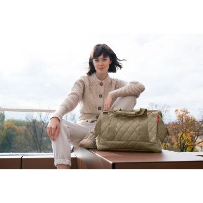 Reisetasche von Reisenthel, Modell Allrounder M, in Olivbeige mit rautenförmiger Steppung, von einer Person an den Tragegriffen getragen.
